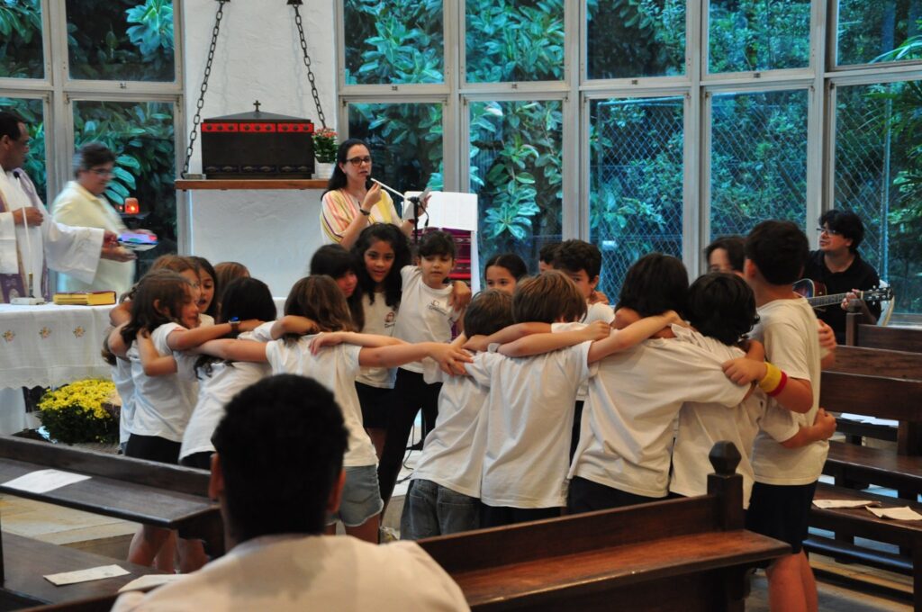 Grupo de crianças do ensino fundamental, todas abraçadas em rola, na capela do Colégio Teresiano durante a disciplina de Educação Religiosa.