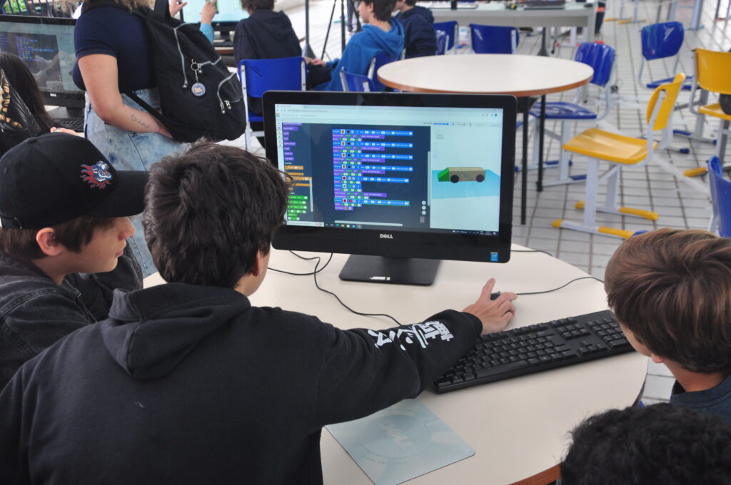 Três alunos trabalham juntos no computador em um projeto de programação.